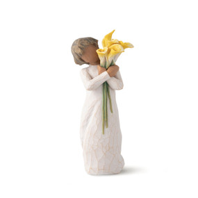 Front view of standing figure in cream dress with darker skin holding yellow calla lilies in her arms
