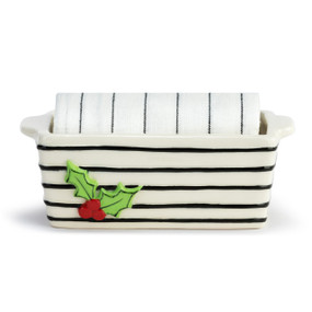 White stoneware loaf pan with black horizontal lines and a raised holly berry image on the side. There is a white tea towel with thin black stripes rolled and placed inside the pan.