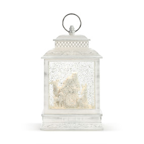 A whitewashed lit lantern with a white nativity scene inside.