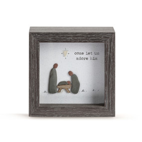 A square dark wood shadow box with a nativity scene and says "come let us adore him" made from glass pebbles.