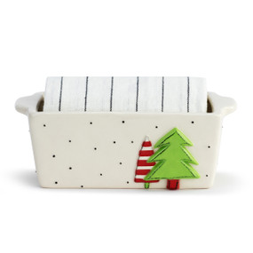 White stoneware loaf pan with black dots and a raised image of two trees on the side. There is a white tea towel with thin black stripes rolled and placed inside the pan.