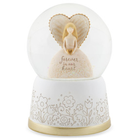 A musical snow globe with an angel figure inside holding a heart that says "forever in our heart". The base is white with a floral scroll pattern.