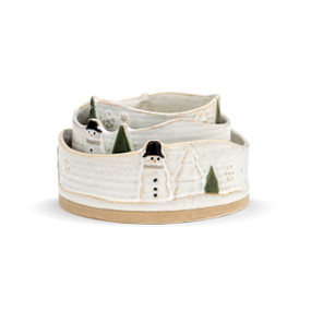 A set of three textured ceramic stacking bowls, each with a winter scene of a snowman, trees, and snowflakes. Stacked inside one another.