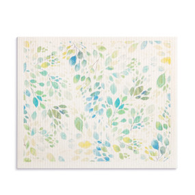 An oversized white biodegradable dish cloth with illustrated pale green, blue and yellow leaves.