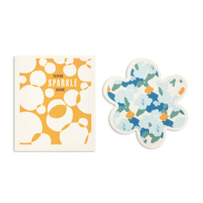 Two blue and orange biodegradable dish cloths. One is flower shaped with illustrated blue flowers and the other is orange and white circles with the saying "Scrub Sparkle Shine".