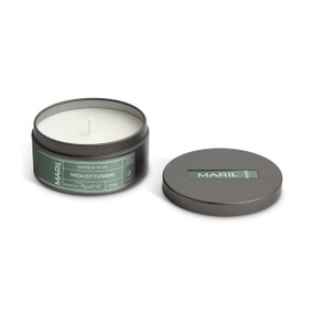 A round dark metal travel tin with a white candle, displayed with the lid off to the side. The candle has a Fresh Cut Flowers scent.