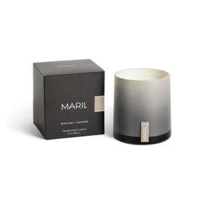 A White Oak + Cashmere poured candle in an ombre gray glass vessel sitting next to a dark gray packaging box.