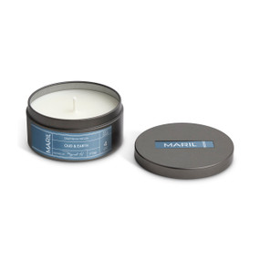 A round dark metal travel tin with a white candle, displayed with the lid off to the side. The candle has an Oud + Earth scent.
