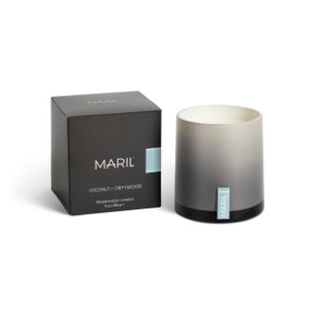 A Coconut + Driftwood poured candle in an ombre gray glass vessel sitting next to a dark gray packaging box.