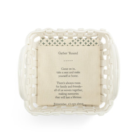 A square white ceramic woven basket with handles on the sides. The basket comes with a cream towel with an inspirational poem on it.
