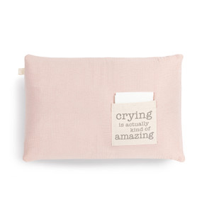 A light pink rectangular pillow with a cream fabric pocket on the front with the saying "crying is actually kind of amazing". The pocket has a white fabric folded in it.