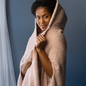 A woman wearing a rose colored hooded wrap standing in front of a blue gray background.