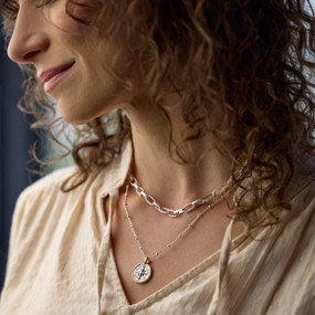 Close up of a woman wearing a cream blouse and a silver multi chain necklace with a round compass pendant.
