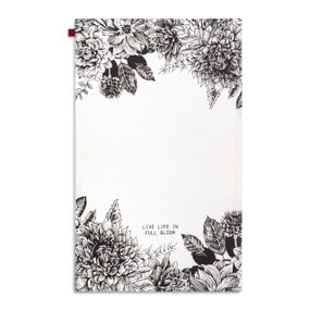 A white kitchen towel with illustrations of black flowers and the saying "Life Life In Full Bloom" displayed with the towel laid out flat.