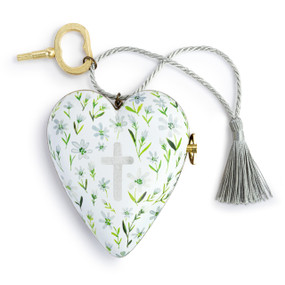 A heart shaped musical sculpture in a white with white and green flowers pattern that has a cross in the middle. The heart has a silver tassel and gold key attached.