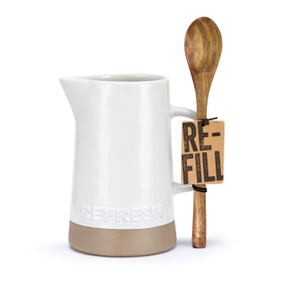 A white ceramic pitcher with a tan textured base and says "Refresh" near the bottom, next to a long wood spoon, displayed with the product tag and spoon attached.