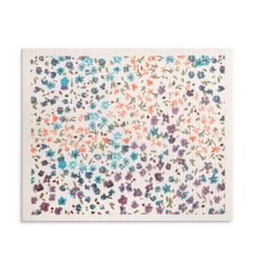 An oversized white biodegradable dish cloth with illustrated small purple, blue and orange flowers.