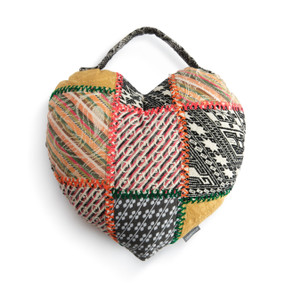 A heart shaped patchwork pillow made up of different multicolored patches. The pillow has a patterned handle at the top.