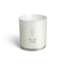 A white glass candle that says "by my side" and has a small white angel wing on the front.