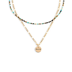 A layered necklace made up of a gold chain with a round gold charm that says "Journey" and a layer of multicolored small beads.
