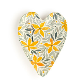 A white heart shaped ceramic spoon rest with a yellow and gray floral illustration on it.