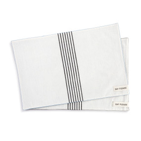 A set of two cream fabric placemats with seven vertical black stripes in the middle. Each has a small fabric tag in the bottom right corner that says "Say Please".