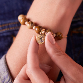 Close up view of a wood bead bracelet on a woman's wrist. The bracelet has a charm that says "Believe Achieve".
