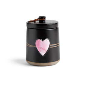 A round black ceramic poured candle with a tan textured base, a lid and a pink raised heart on the front.