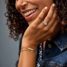 Close up of a smiling woman wearing a multi layered gold chain bracelet with a bar that says "Follow Your Heart".