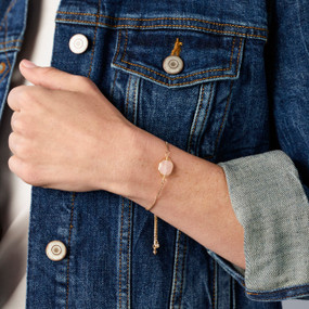 Close up of a gold chain bracelet with a rose stone charm.