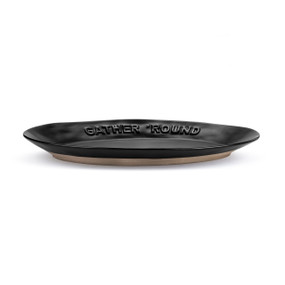 A black oval ceramic platter with a tan textured base. The rim of the platter says "Gather 'Round".