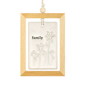 A hanging cream ceramic plaque with flowers and the word "family" suspended inside a light wood open frame.