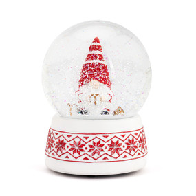 A musical snow globe with a red and white snowflake base, a sitting gnome inside holding a present and wearing and red and white striped hat.