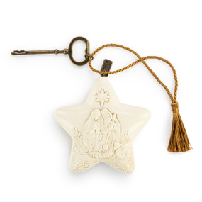 A cream star shaped sculpture with a sculpted image of the holy family. The star has a gold tassel and gold key attached.