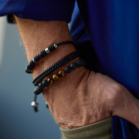 Close up of a man wearing three different black leather cord and beaded bracelets.