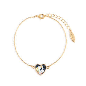 An adjustable gold chain bracelet with a heart shaped charm of white flowers on a dark blue background.