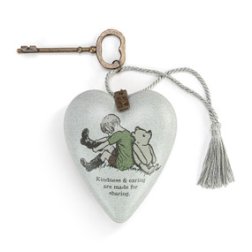 Heart shaped sculpture with a silver tassel and metal key attached. The heart has the image of Pooh and Christopher Robin on a gray background and says "Kindness & caring are made for sharing".