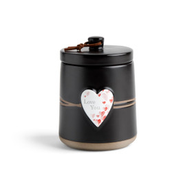 A round black ceramic poured candle with a tan textured base, a lid and a white raised heart on the front with a red heart illustration and the words "Love You".