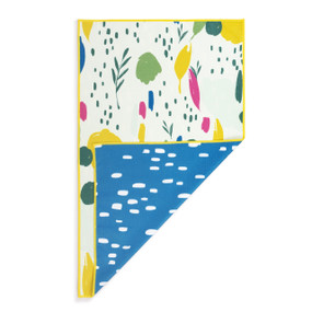 A rectangular double sided towel. One side is white with a colorful modern illustration and the other is blue with white spots, displayed with the blue corner turned back.