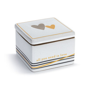 A white square ceramic keepsake box with stripes at the base and a lid. The lid has two hearts and the box says "all you need is love" near the bottom, displayed angled to the right.