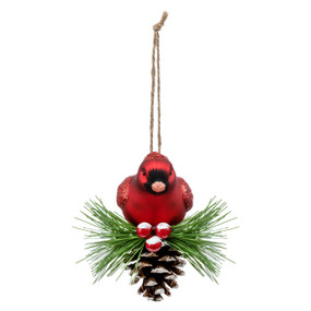 A red cardinal bird ornament with the bird sitting on a snowy pinecone and evergreen branch.