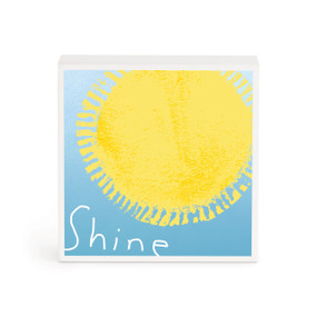 A small white box artwork of a yellow sun on a blue background and the word "Shine" in white.