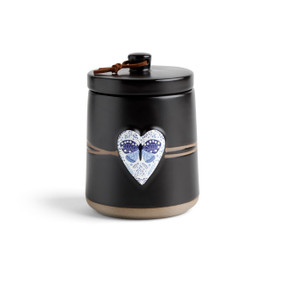 A round black ceramic poured candle with a tan textured base, a lid and a white raised heart on the front with the image of a blue butterfly.