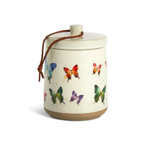 A cream ceramic candle with a tan textured base and watercolor butterflies on the outside with a removable lid.
