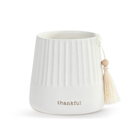 A small round white ceramic cachepot with "thankful" on the front with a cream tassel.