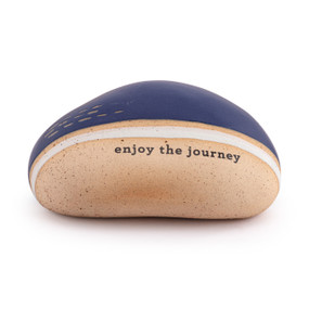 A dark blue and tan stoneware rock that says "enjoy the journey".
