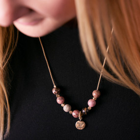 Close up of a woman in a black top wearing a silver chain necklace with seven pink and gold beads for habit tracking.