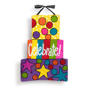 A reversible metal door hanger in the shape of a stack of 3 gifts, decorated with bright colorful dots and says "Celebrate!".