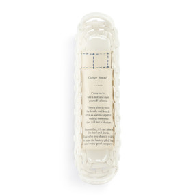 A long white ceramic woven basket with handles at the ends. The basket comes with a cream towel with an inspirational poem on it.