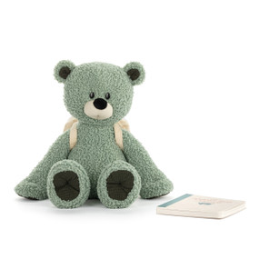 A green plush bear wearing a cream backpack and a paper journal set next to him.
